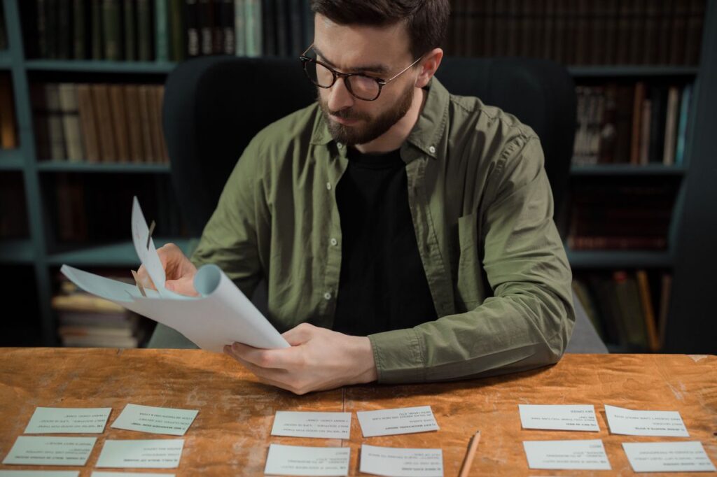 Adult male studying papers in a library setting, focusing on education and research.